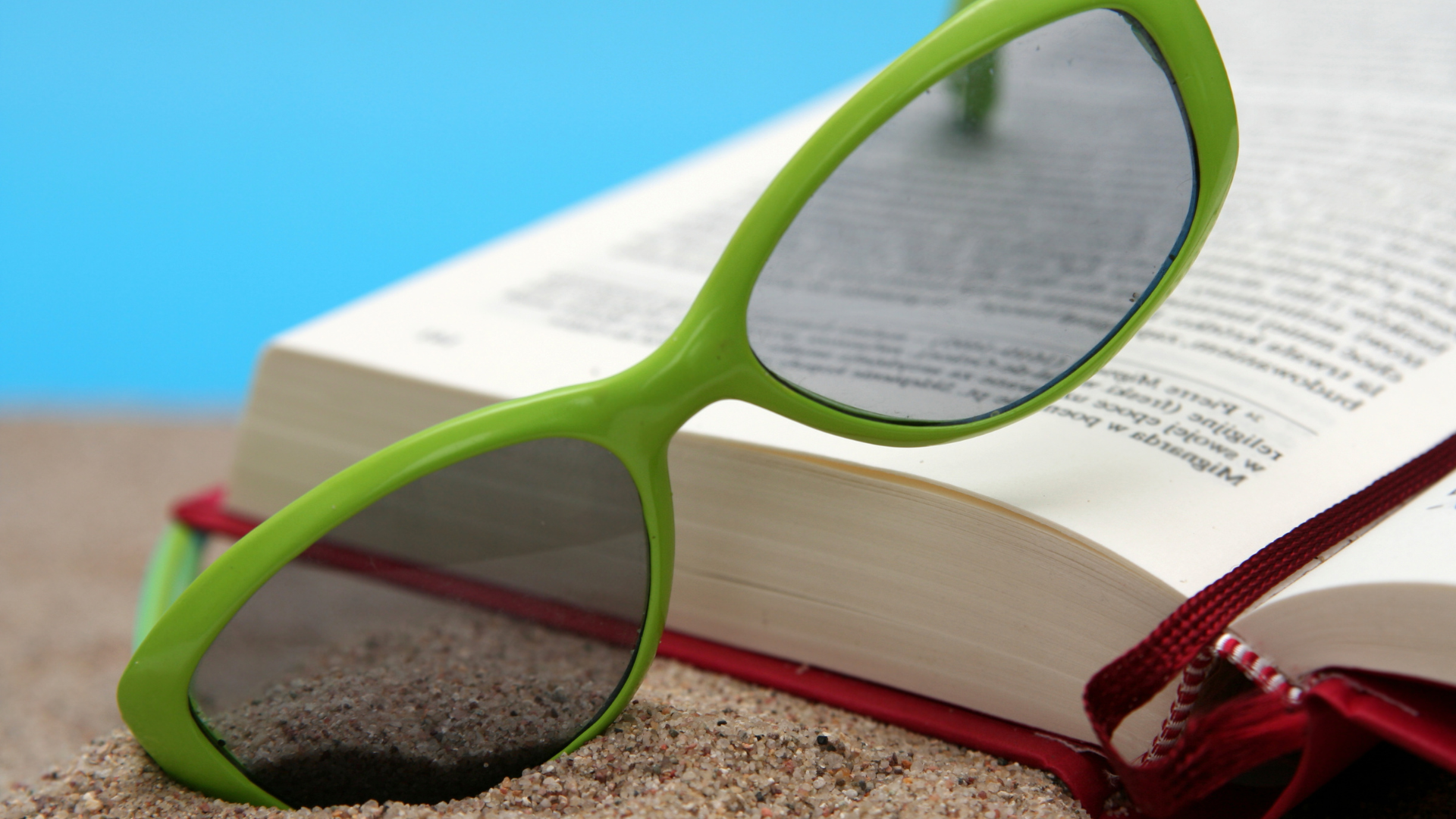 pair of green sunglasses propped on an open book lying on the beach