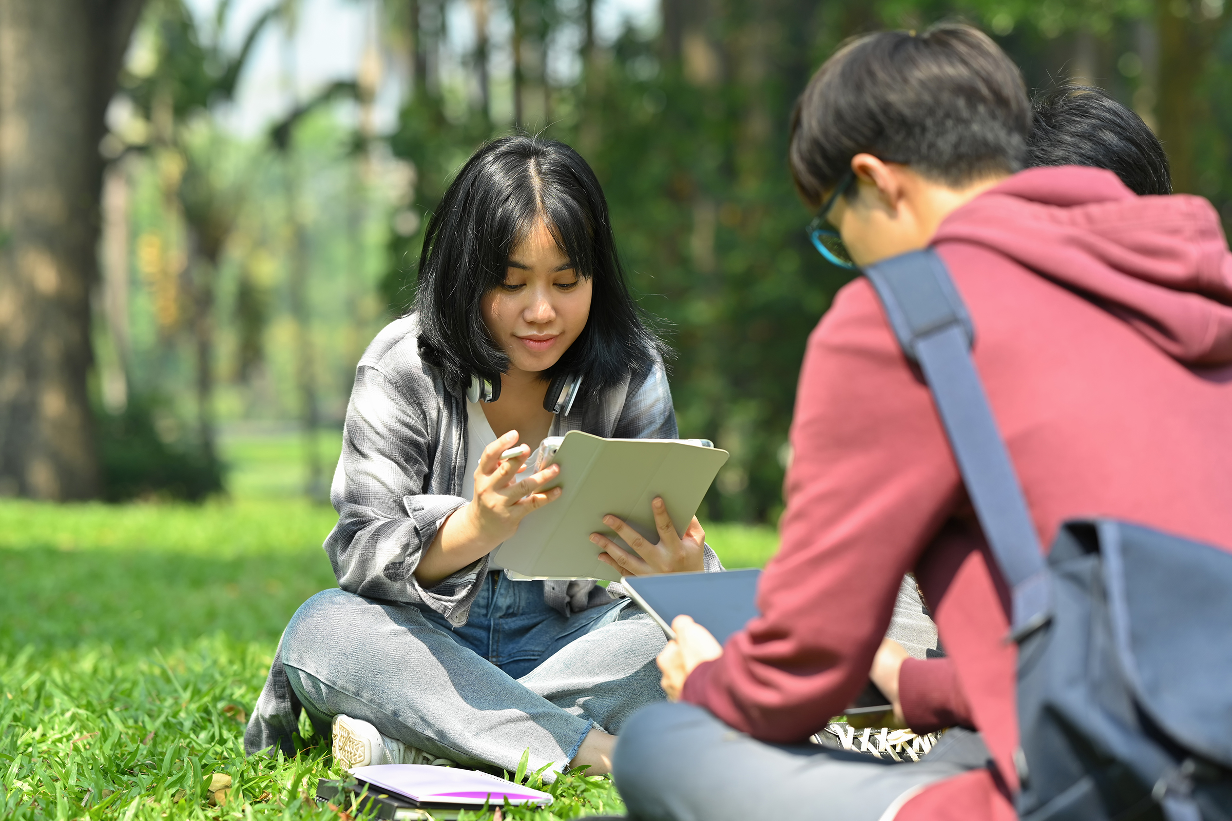 Image of asian female student reading books with her friends at summer park.