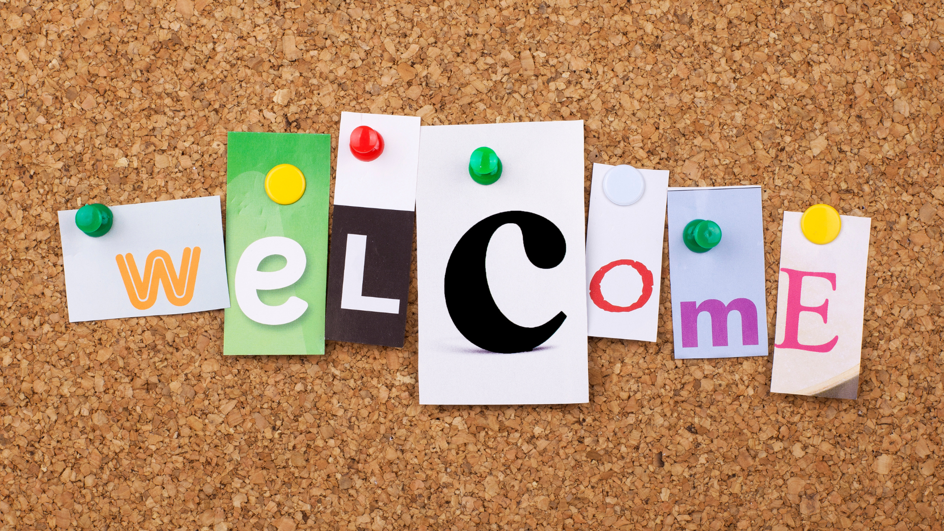 scraps of paper pinned to a cork board spelling out welcome